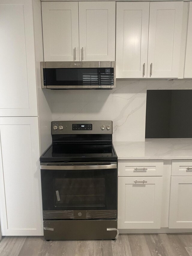 kitchen with white cabinets, light hardwood / wood-style floors, light stone counters, and appliances with stainless steel finishes