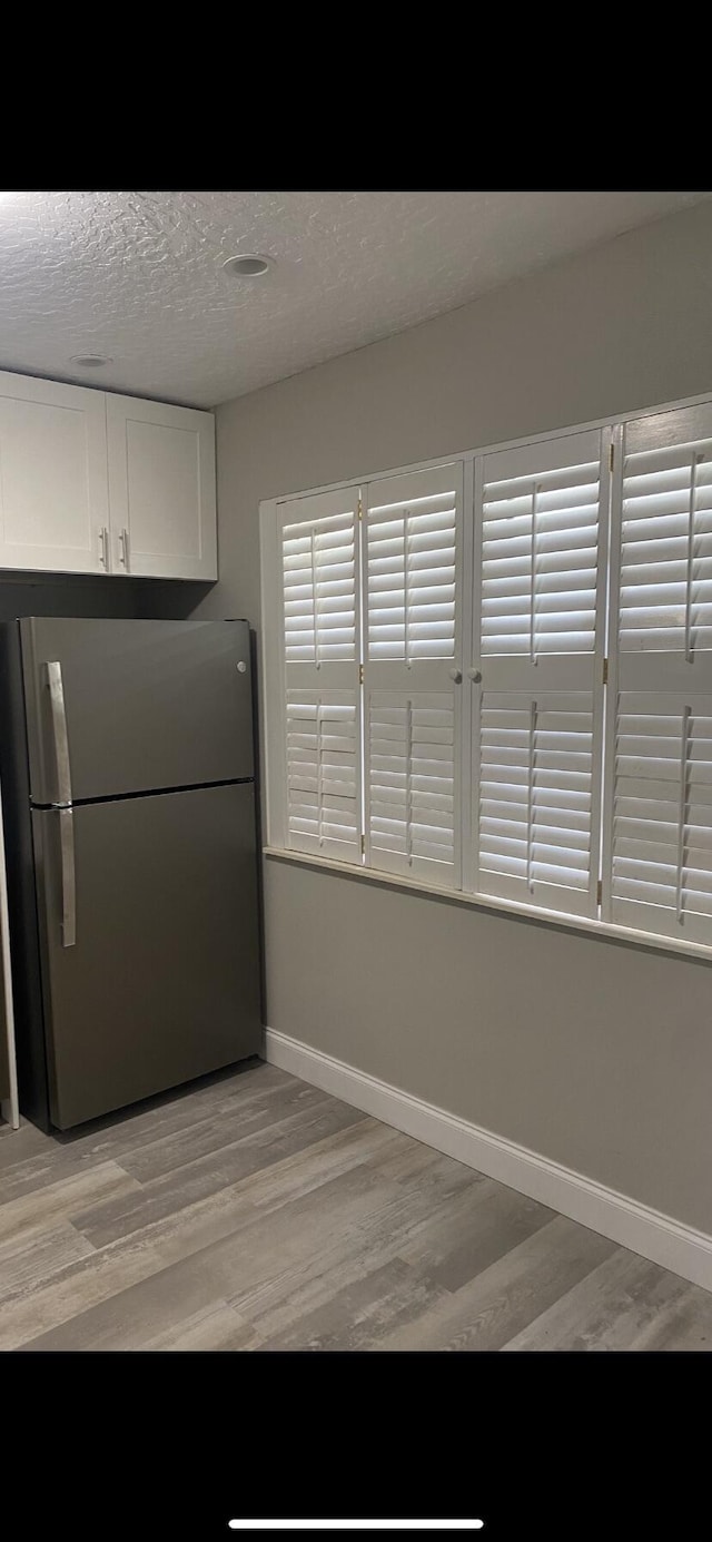 kitchen with a textured ceiling, stainless steel refrigerator, white cabinetry, and light hardwood / wood-style flooring