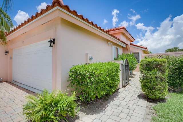 view of side of home with a tile roof, an attached garage, and stucco siding