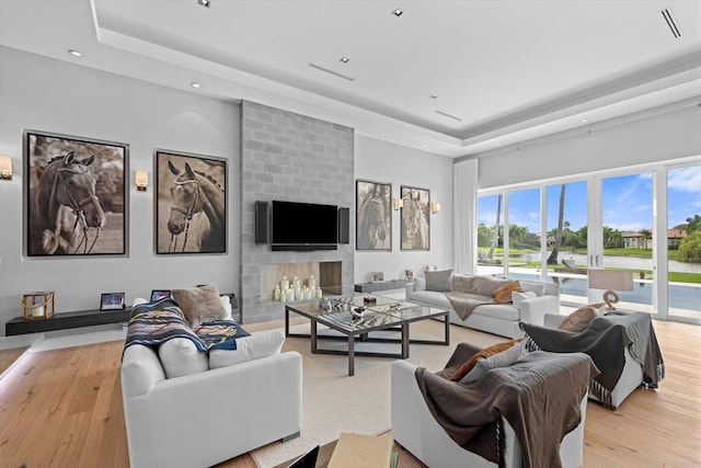 living room with a large fireplace, a tray ceiling, and light hardwood / wood-style floors