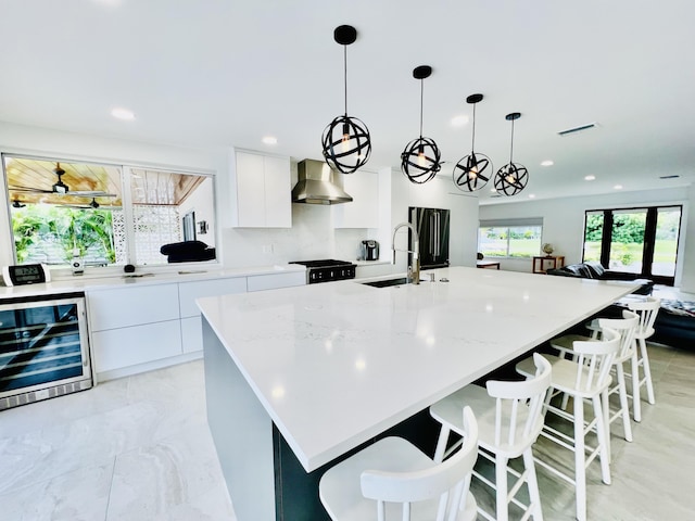 kitchen with a large island with sink, white cabinetry, wall chimney exhaust hood, and hanging light fixtures