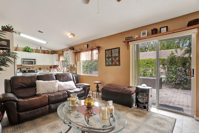 living room with ceiling fan, a textured ceiling, vaulted ceiling, and light tile patterned floors