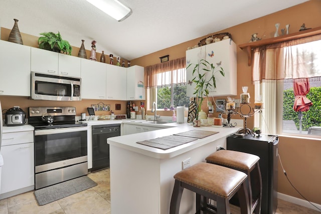 kitchen with lofted ceiling, kitchen peninsula, light tile patterned floors, stainless steel appliances, and sink