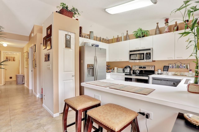 kitchen featuring a breakfast bar area, appliances with stainless steel finishes, light tile patterned floors, white cabinets, and kitchen peninsula