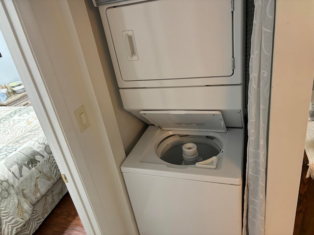 laundry area featuring stacked washer / dryer and dark wood-type flooring