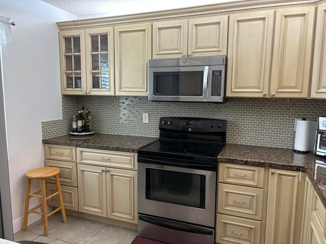 kitchen featuring appliances with stainless steel finishes, light tile patterned flooring, cream cabinetry, and backsplash