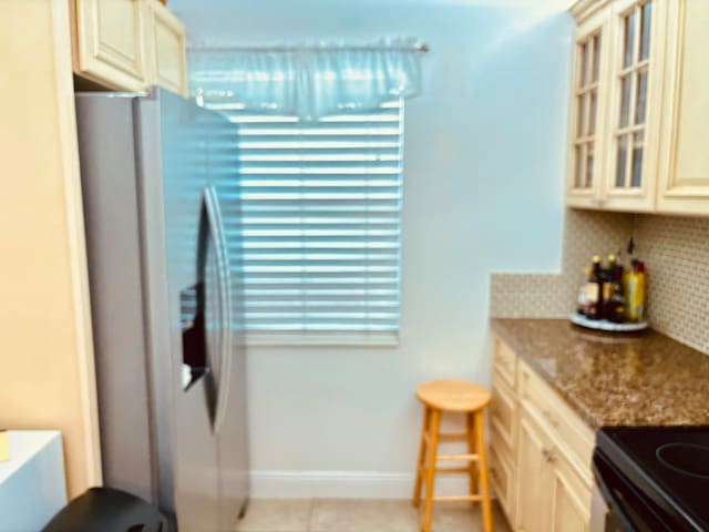 kitchen with stainless steel fridge with ice dispenser, cream cabinetry, tasteful backsplash, and light stone countertops