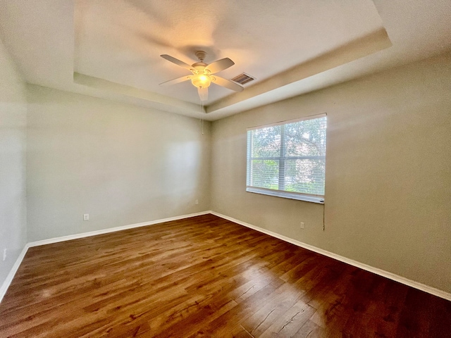 unfurnished room with hardwood / wood-style floors, ceiling fan, and a raised ceiling