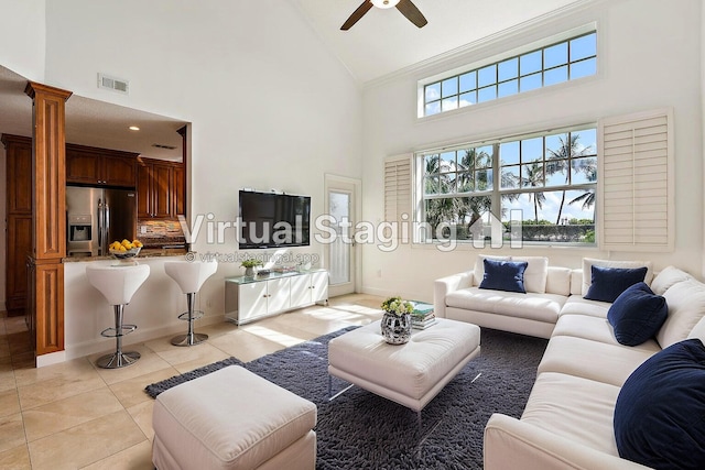 tiled living room with decorative columns, high vaulted ceiling, crown molding, and ceiling fan