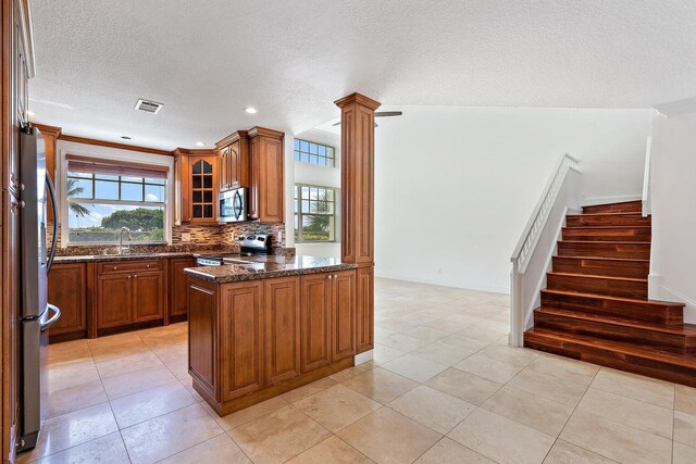 kitchen featuring tasteful backsplash, appliances with stainless steel finishes, a textured ceiling, dark stone counters, and sink