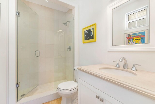 bathroom featuring hardwood / wood-style flooring, a shower with door, toilet, and vanity