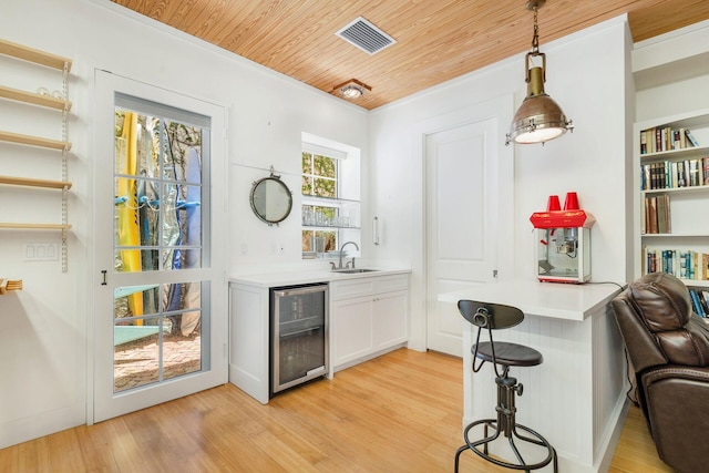 bar featuring beverage cooler, light wood finished floors, visible vents, and decorative light fixtures