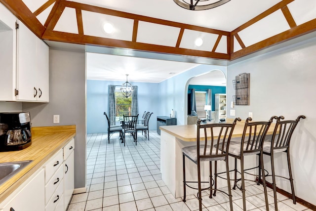 kitchen featuring white cabinetry, a kitchen bar, a notable chandelier, light tile patterned flooring, and pendant lighting