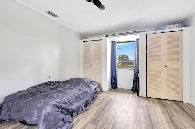 bedroom with ceiling fan, two closets, a textured ceiling, and light wood-type flooring