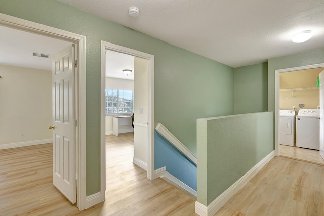 hall featuring light hardwood / wood-style flooring, a textured ceiling, and washer and clothes dryer