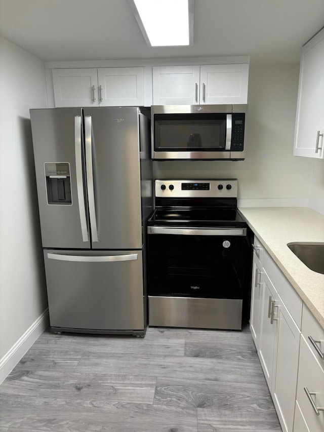 kitchen with appliances with stainless steel finishes, light hardwood / wood-style flooring, and white cabinetry