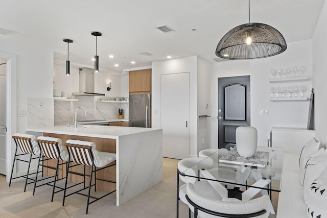 kitchen featuring decorative light fixtures, high end refrigerator, kitchen peninsula, and wall chimney exhaust hood