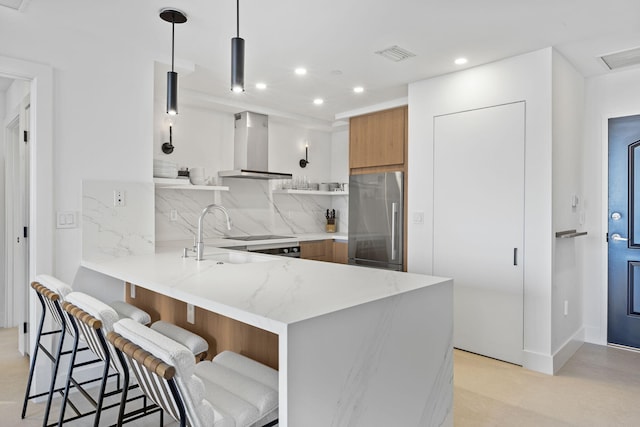 kitchen featuring pendant lighting, a breakfast bar area, high end refrigerator, kitchen peninsula, and wall chimney exhaust hood