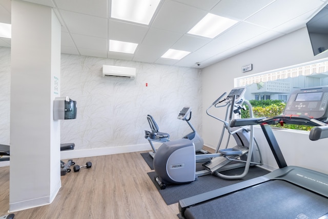 workout area featuring a drop ceiling, a wall mounted air conditioner, and light wood-type flooring