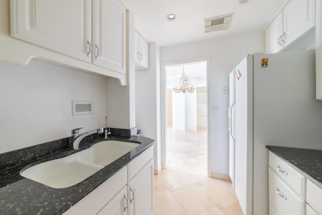 kitchen with white cabinets, light tile patterned floors, dark stone counters, white fridge, and sink