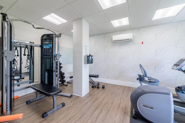 exercise room featuring light hardwood / wood-style floors, a wall mounted AC, and a paneled ceiling