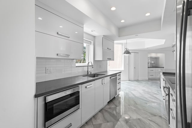 kitchen with stainless steel appliances, sink, pendant lighting, light tile patterned floors, and a tray ceiling