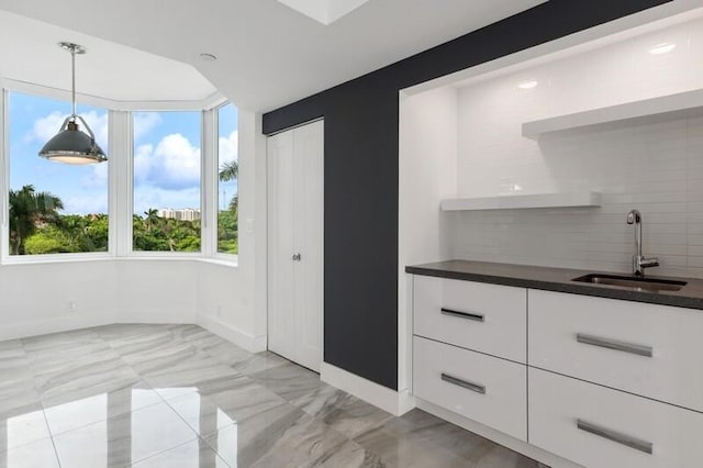 kitchen with tasteful backsplash, light tile patterned floors, white cabinets, decorative light fixtures, and sink