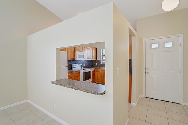 kitchen with tasteful backsplash, white appliances, vaulted ceiling, and light tile patterned floors