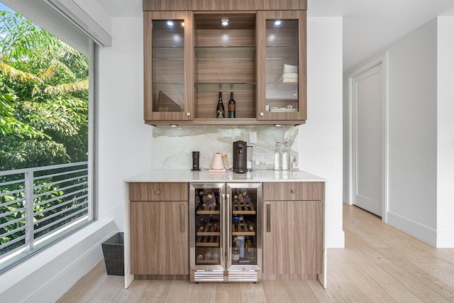 bar with beverage cooler, baseboards, light wood-type flooring, decorative backsplash, and a bar