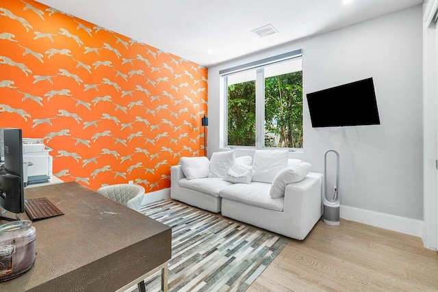 living area with an accent wall, light wood-type flooring, baseboards, and wallpapered walls