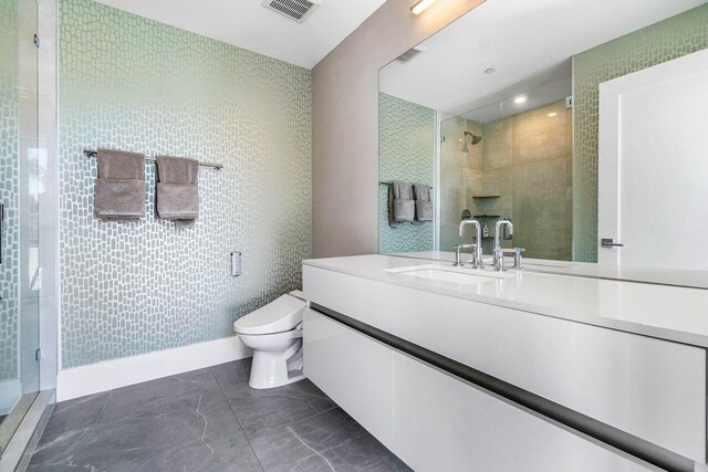 bathroom with vanity, tiled shower, toilet, and tile patterned flooring