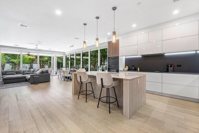 kitchen featuring white cabinets, a spacious island, modern cabinets, a breakfast bar, and pendant lighting