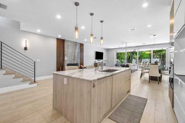 kitchen with a large island, modern cabinets, light stone counters, open floor plan, and a sink