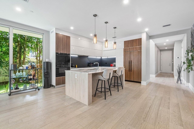 kitchen featuring light stone counters, an island with sink, a kitchen bar, and modern cabinets