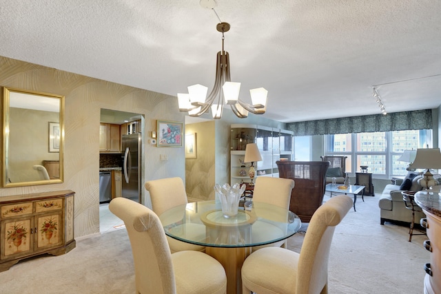 dining space with a chandelier, a textured ceiling, light colored carpet, and track lighting