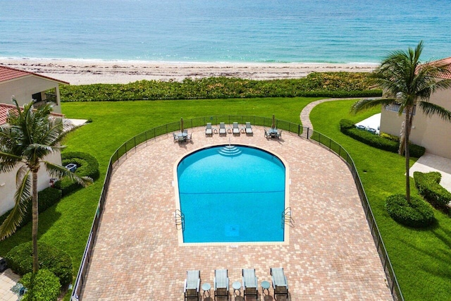 view of swimming pool with a beach view, a lawn, and a water view