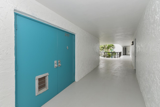 corridor featuring concrete flooring and a textured wall