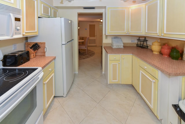 kitchen with cream cabinetry, light tile patterned floors, and white appliances