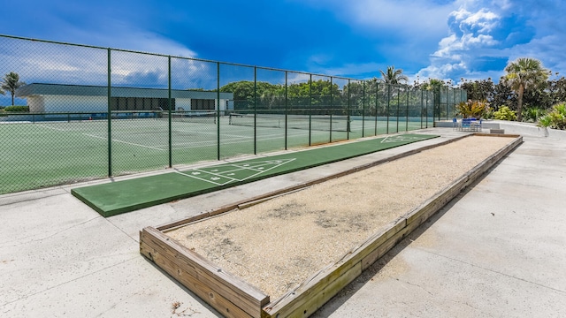 view of community with a tennis court, fence, and shuffleboard