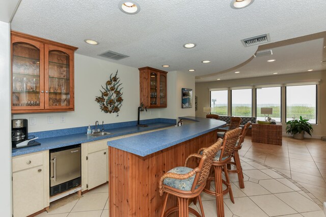 kitchen with stainless steel dishwasher, sink, a breakfast bar, a textured ceiling, and light tile patterned floors