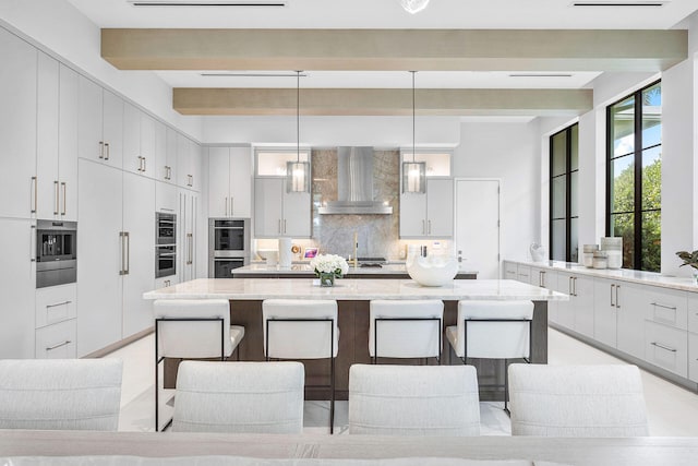 kitchen with wall chimney range hood, tasteful backsplash, decorative light fixtures, a kitchen bar, and a spacious island