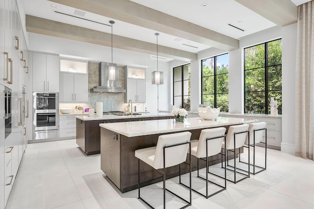 kitchen with a center island, wall chimney exhaust hood, sink, pendant lighting, and backsplash