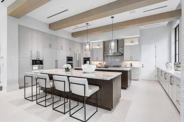 kitchen with beamed ceiling, decorative backsplash, wall chimney exhaust hood, pendant lighting, and a spacious island