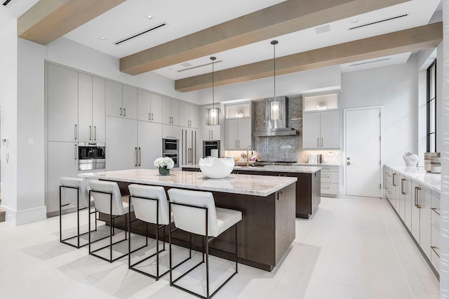 kitchen with wall chimney range hood, a spacious island, pendant lighting, decorative backsplash, and light stone counters