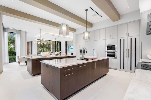 kitchen with hanging light fixtures, a kitchen island with sink, beam ceiling, and dark brown cabinets