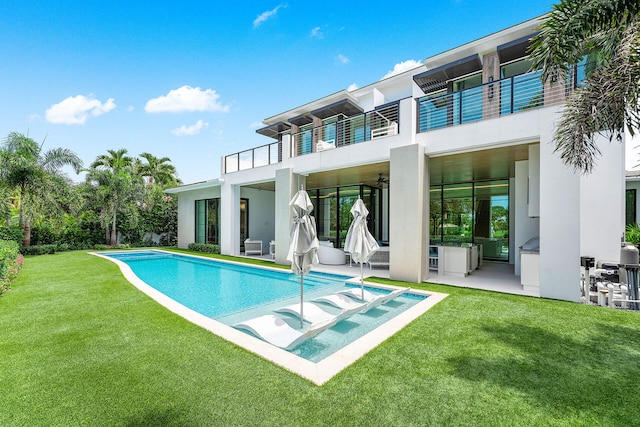 rear view of property featuring a patio, a pool with hot tub, a balcony, and a lawn