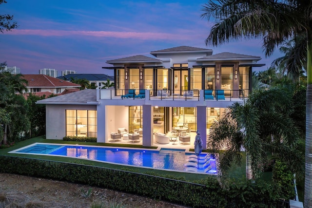 back house at dusk with a pool with hot tub, a patio area, and a balcony