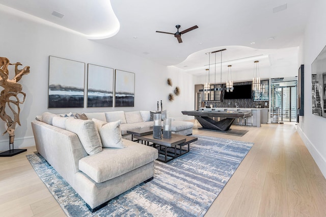 living room featuring ceiling fan with notable chandelier and light hardwood / wood-style flooring