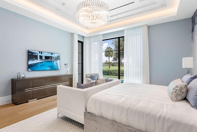 bedroom with an inviting chandelier, hardwood / wood-style floors, and a raised ceiling