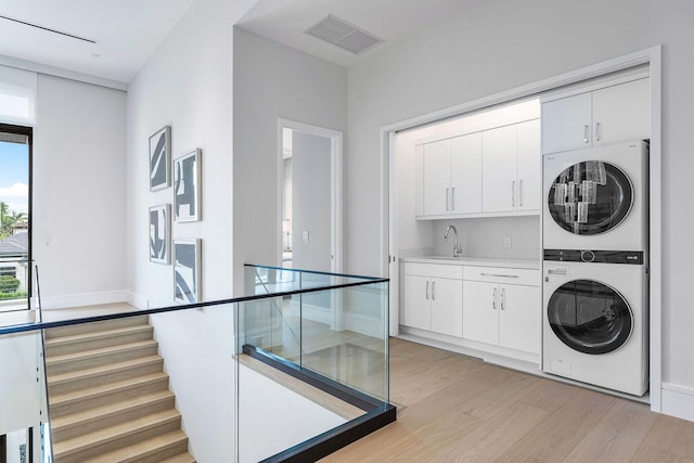 laundry area with cabinets, sink, light hardwood / wood-style flooring, and stacked washer / drying machine